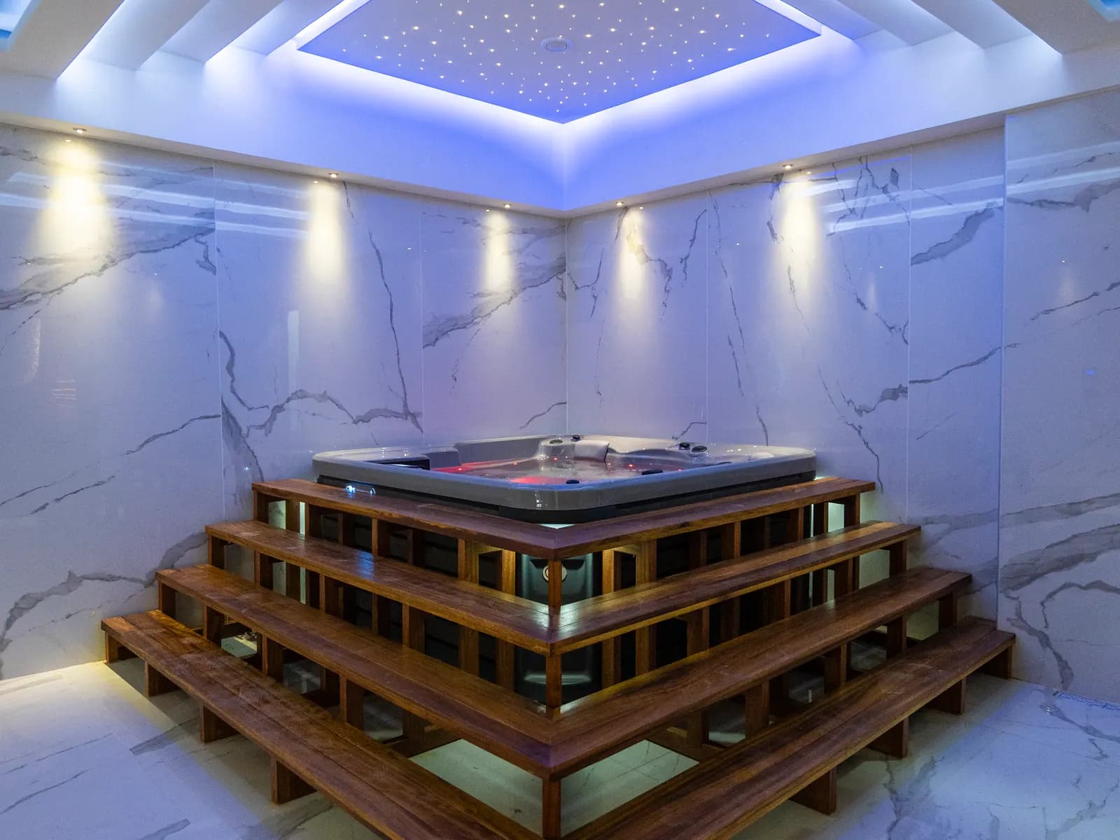 Mermer kaplı spa odasında basamaklı ahşap platforma oturtulmuş jakuzi.